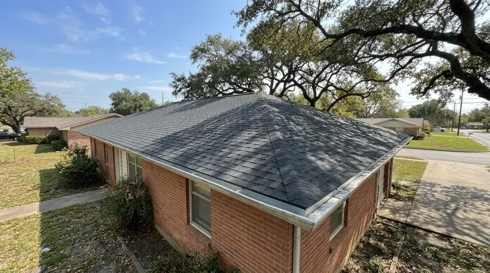 Older brick home with a hip shingle roof under live oak trees